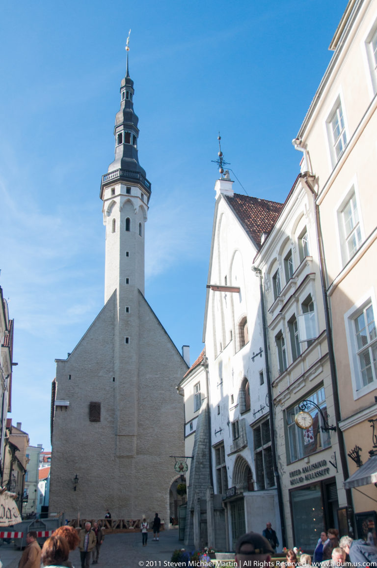 Tallinn Town Hall tower with pale masonry shaft and dark spire rising above the square and surrounding historic façades.