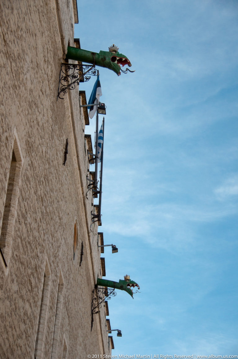Upward view of green dragon-shaped rainwater spouts projecting from Tallinn Town Hall against a blue sky.