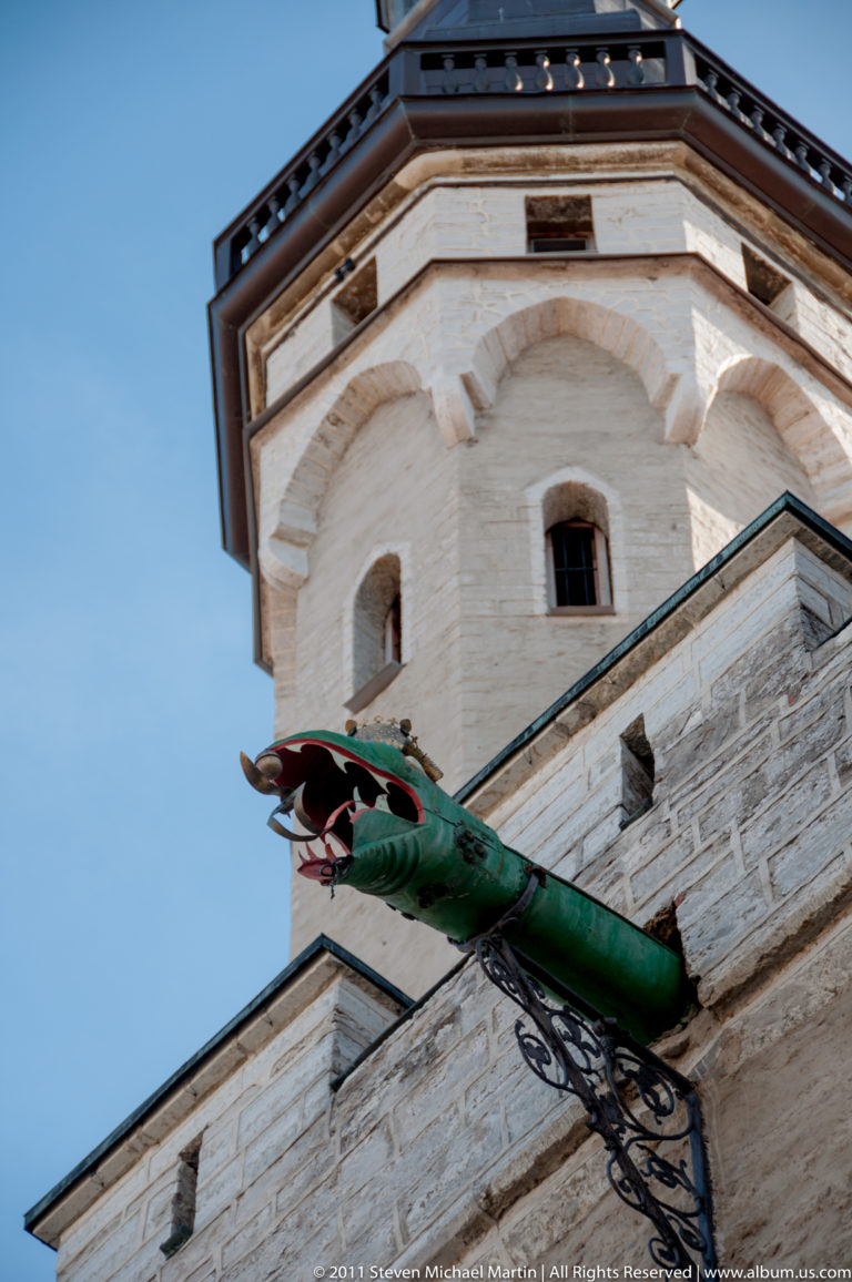 Low-angle view of a green dragon-shaped rainwater spout projecting from the pale stone wall of Tallinn Town Hall.