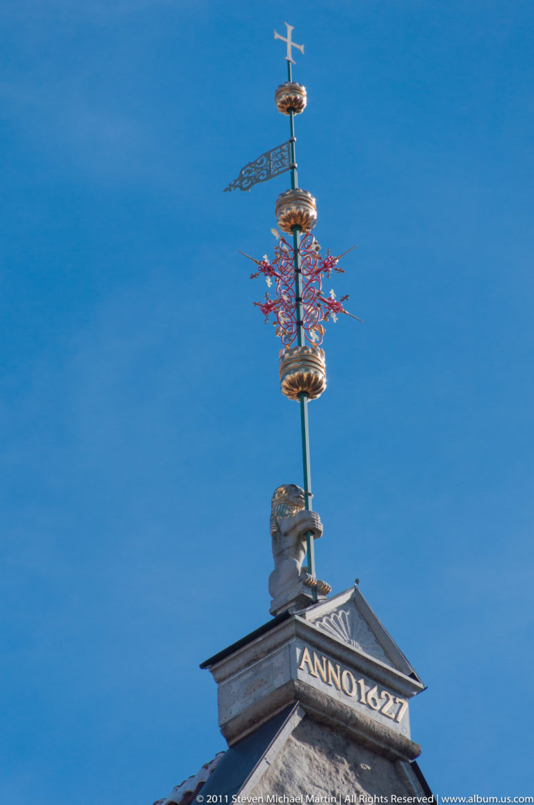 Ornamental rooftop finial above a pediment inscribed “ANNO 1427” against a deep blue sky.