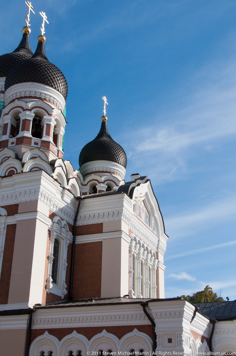 Oblique side view of Alexander Nevsky Cathedral showing dark onion domes, gilded crosses, white trim, and red-brown walls.