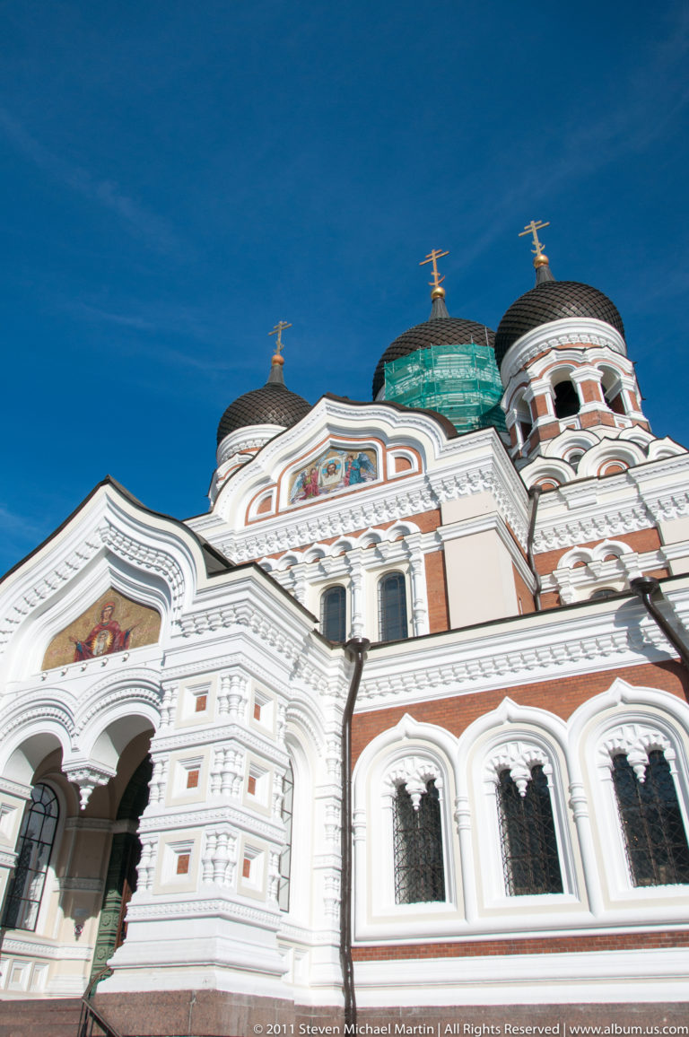 Alexander Nevsky Cathedral in Tallinn with ornate white-and-red façade, dark onion domes, mosaic icons, and gilded Orthodox crosses.