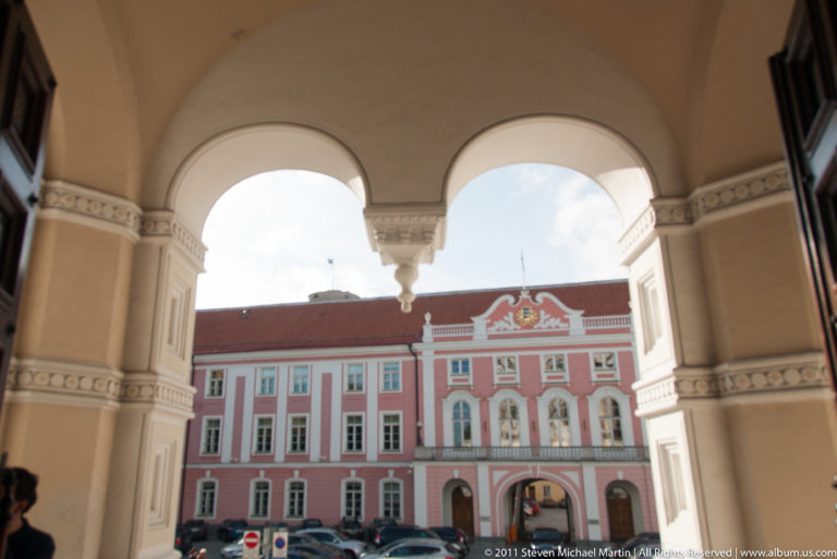 Pink-and-white historic façade framed by a large cream-colored arched passage in Tallinn’s upper town.