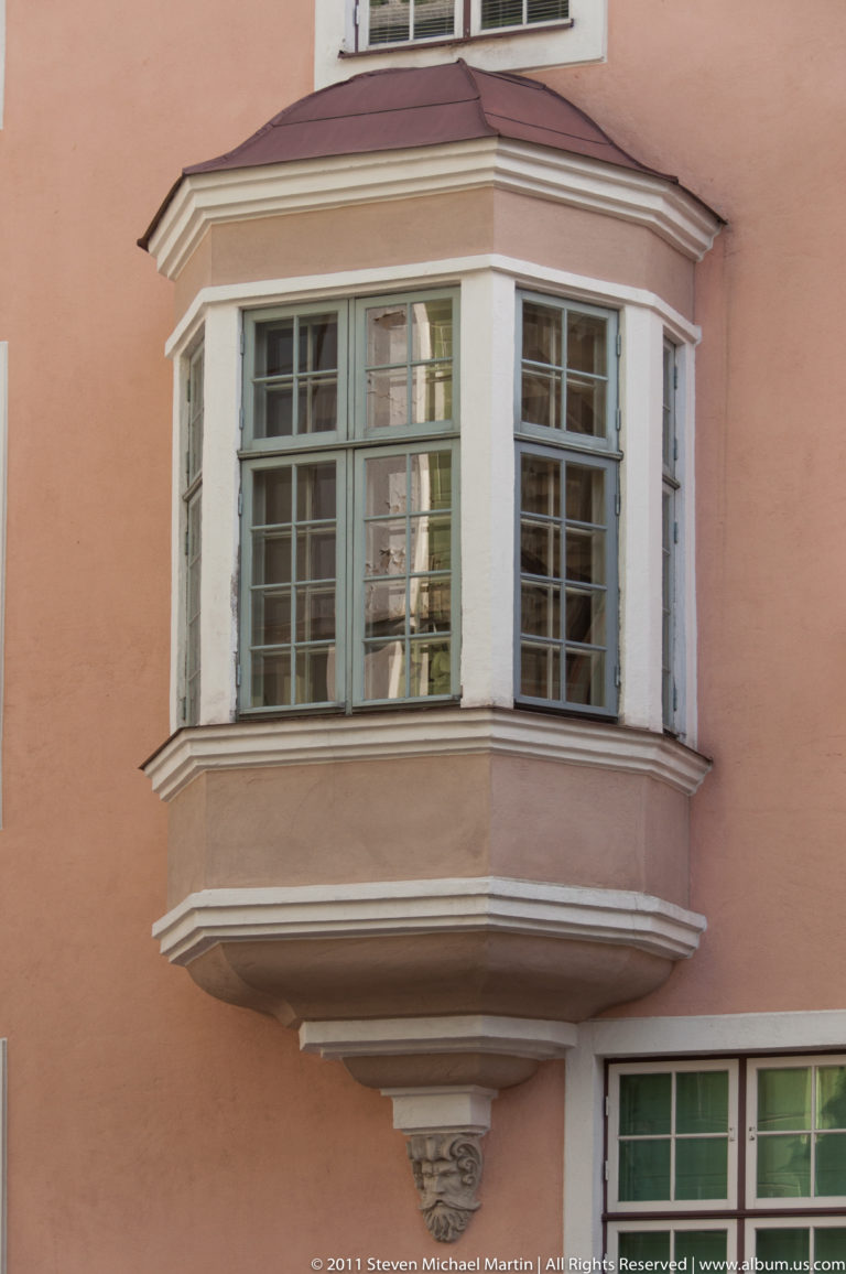 White-framed projecting bay window with many small panes on a salmon-colored historic building in Tallinn.