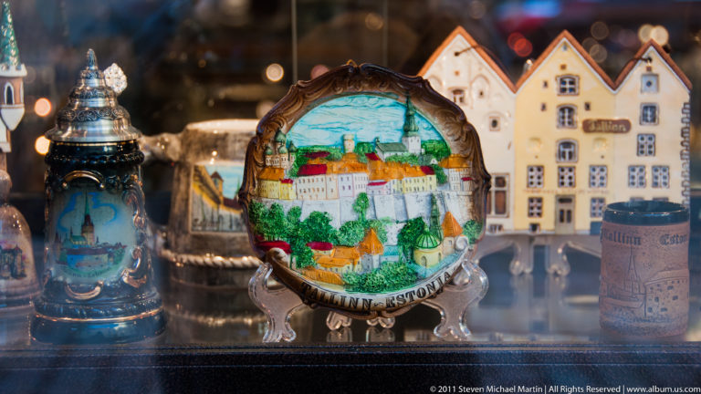 Painted Tallinn souvenir plate displayed among decorative beer steins and miniature gabled buildings.