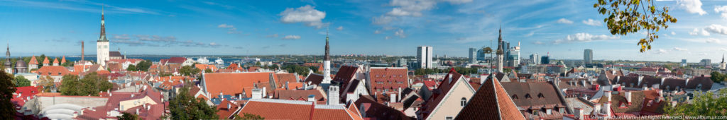 Broad elevated view of Tallinn Old Town with church spires, red roofs, and modern high-rises in the distance.