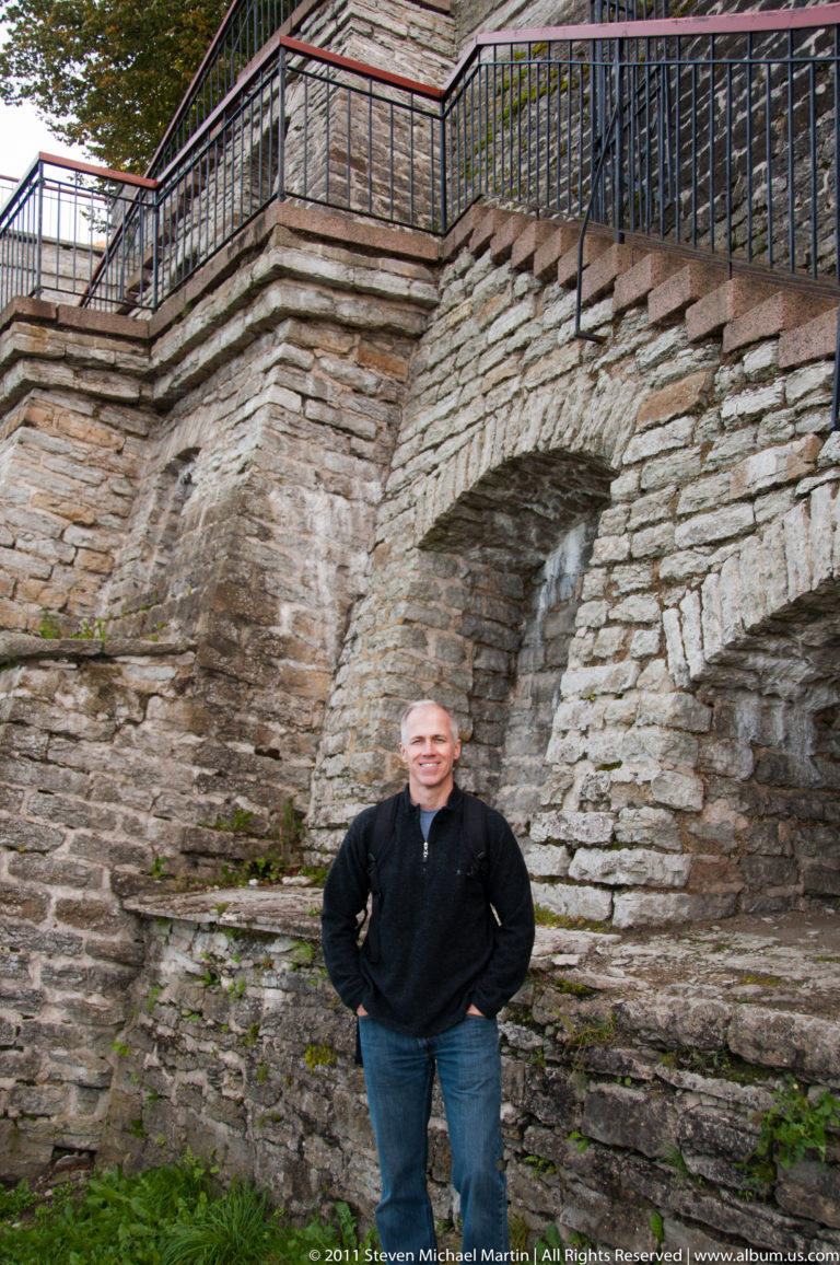 Adult standing beneath heavy stone arches in Tallinn’s historic fortifications, with railings along the upper level.