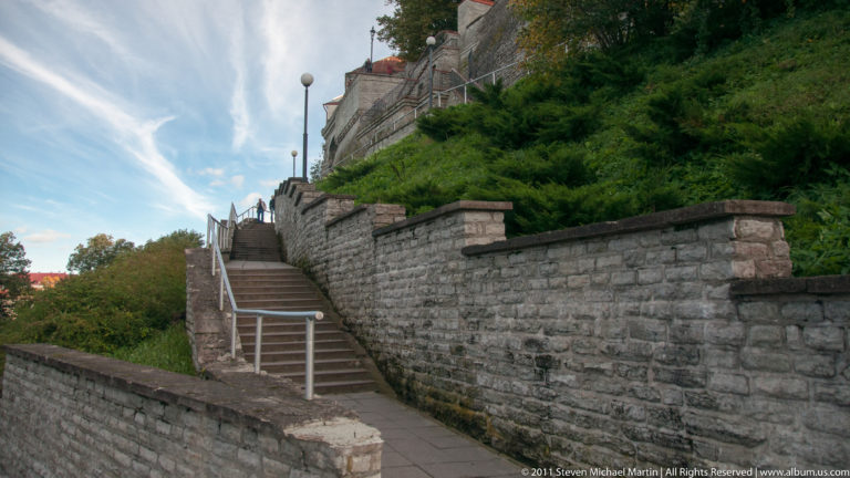 Stone stairway climbing between masonry retaining walls and green slopes in Tallinn’s historic center.