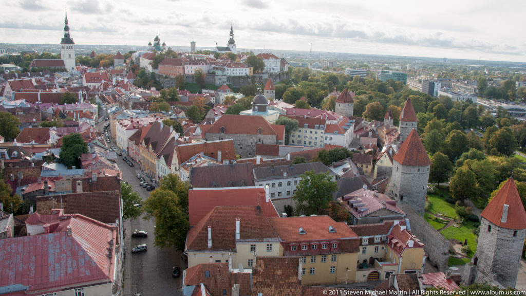 Elevated view of Tallinn Old Town with medieval stone wall towers, red conical roofs, streets, and historic buildings.