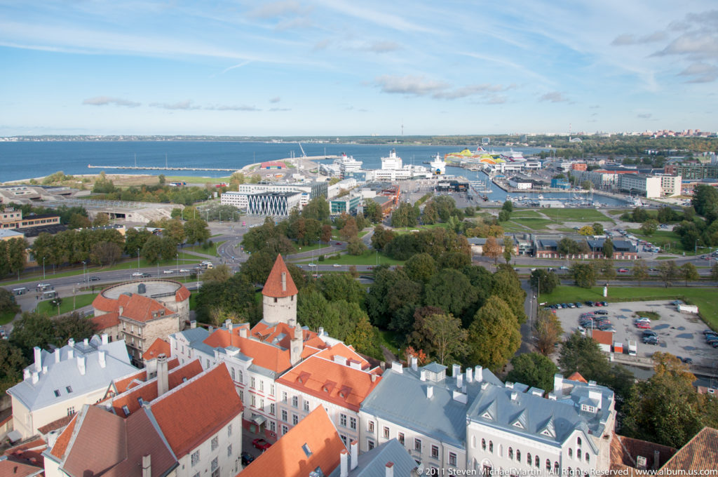 Elevated view from Tallinn Old Town toward the passenger harbor and Baltic shoreline, with red-roofed historic buildings in the foreground.