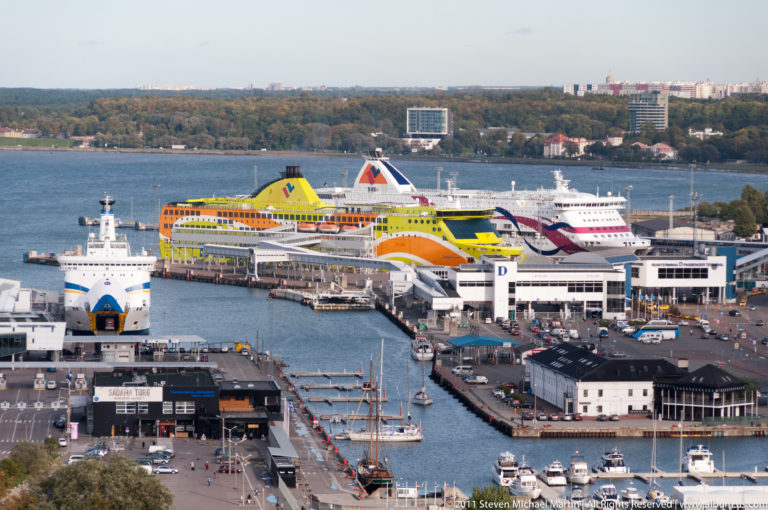 Large passenger ferries docked at Tallinn harbor beside terminal buildings, service quays, ramps, and smaller vessels.