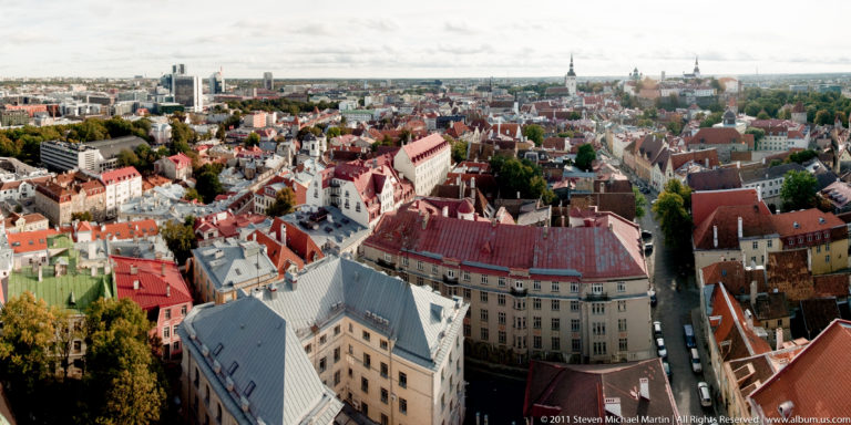 Wide elevated view across Tallinn Old Town rooftops and spires toward the modern city beyond.
