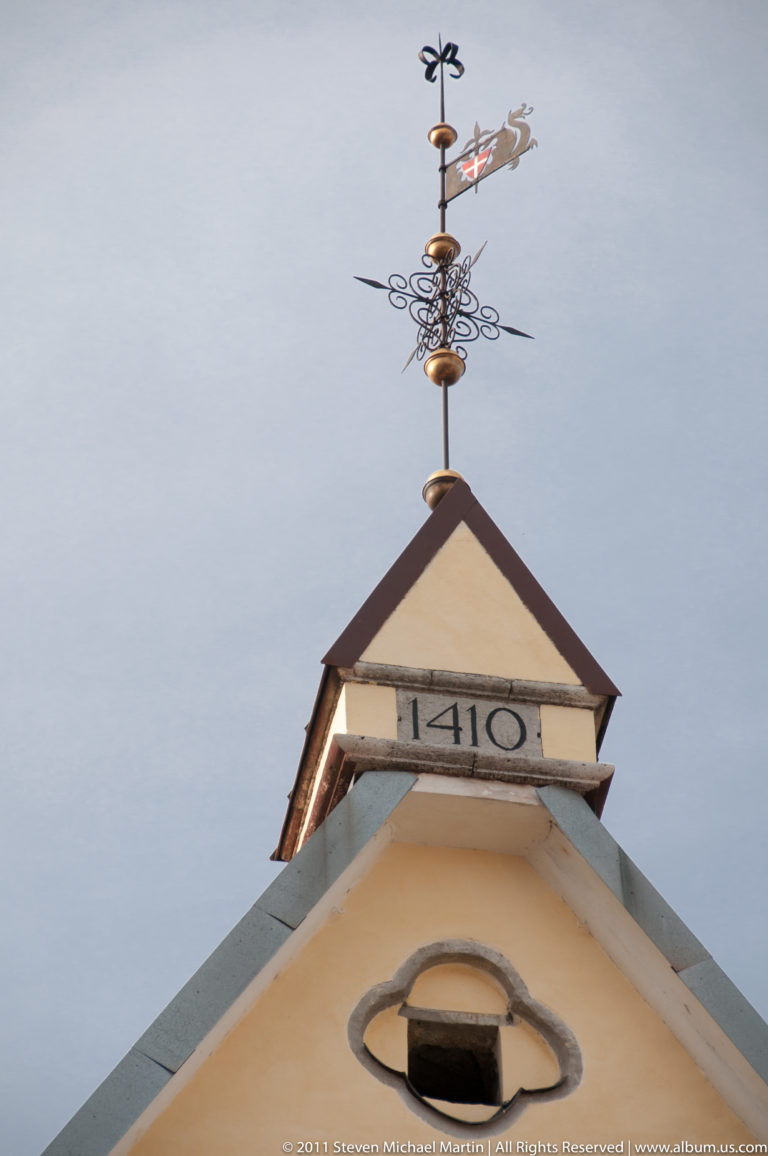 Historic Tallinn gable marked 1410, topped by an ornate metal weather vane with scrollwork and a small figurative finial.