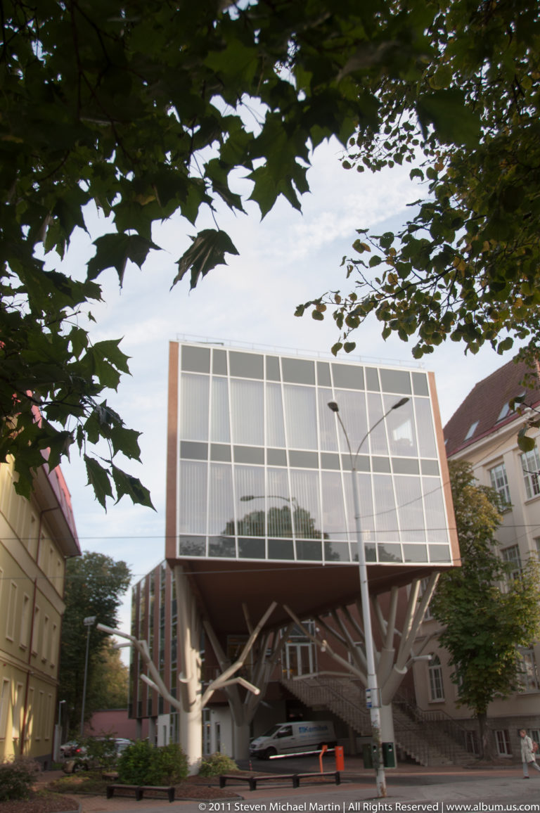 Modern cantilevered glass-and-metal building set between older pitched-roof buildings in Tallinn.