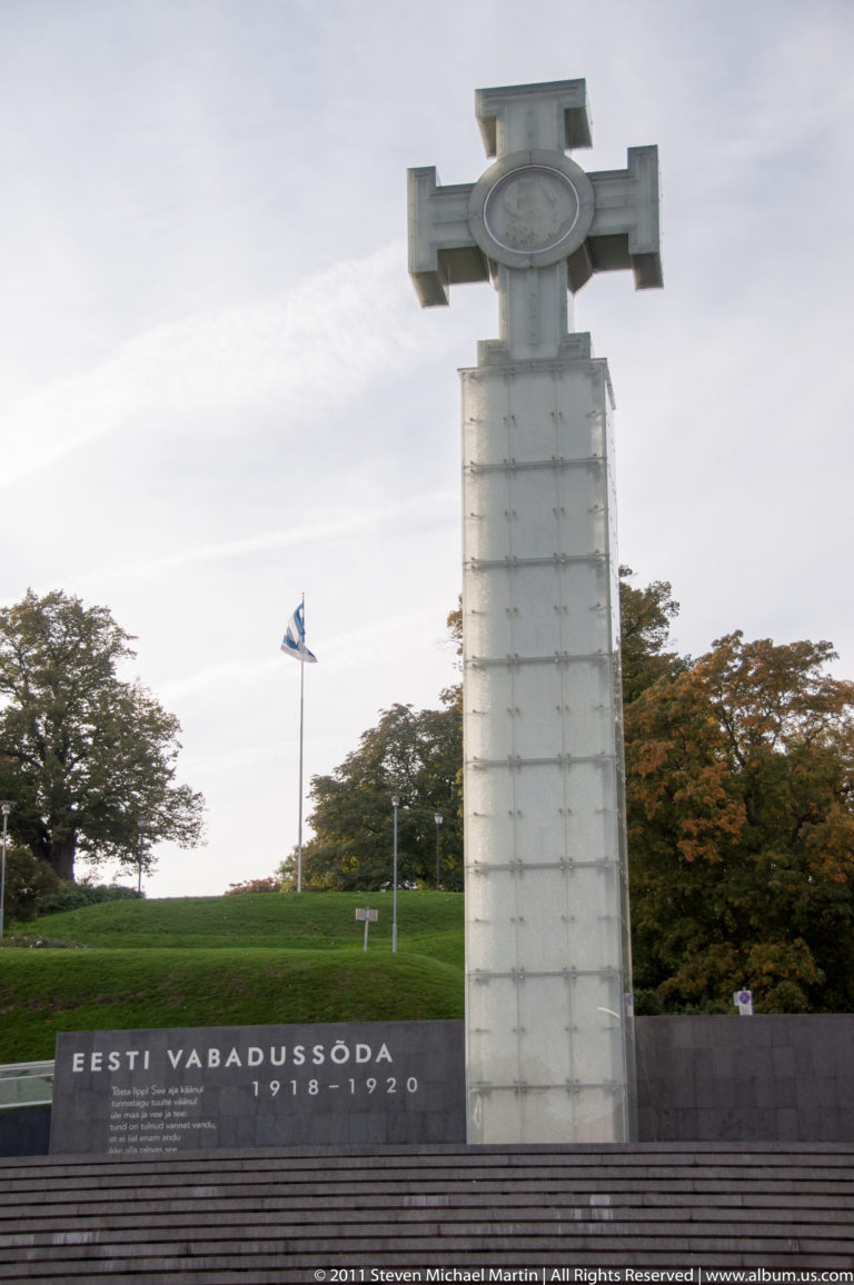 Victory Column at Tallinn Freedom Square with Cross of Liberty, war inscription, and Estonian flag.