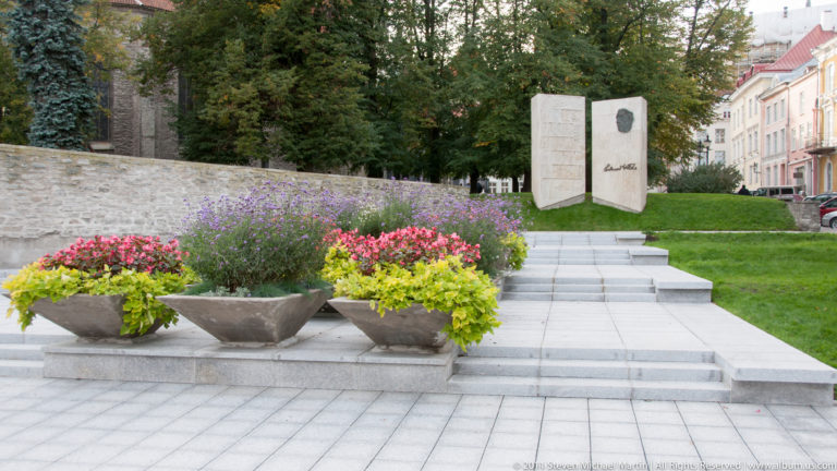 Flower-filled planters and steps leading to the paired stone slabs of the Eduard Vilde memorial.
