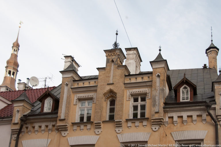 Ornate historic façade with stepped gable, pinnacles, tall windows, dormers, and nearby towers.