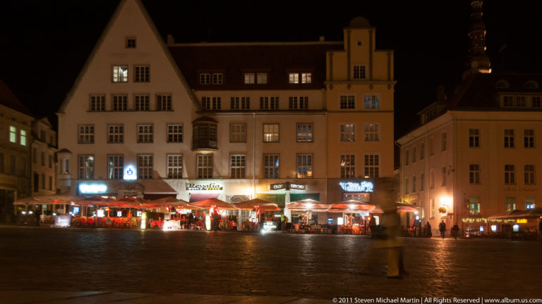Night view across Tallinn Town Hall Square toward restaurant terraces and historic merchant houses.