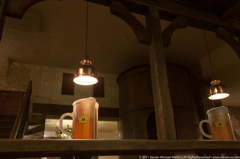 Two large beer mugs on a wooden ledge beneath pendant lamps in a dark timber-framed tavern.