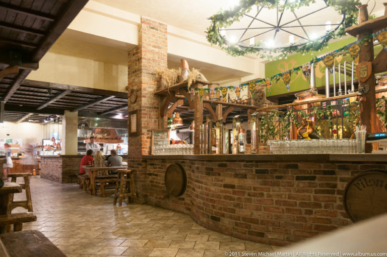 Brick bar, timber details, barrels, and wooden dining tables inside a historic-themed Tallinn restaurant.