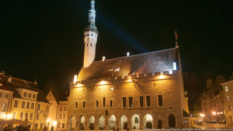 Illuminated Gothic Tallinn Town Hall at night with steep roof, pointed arches, and tall tower.