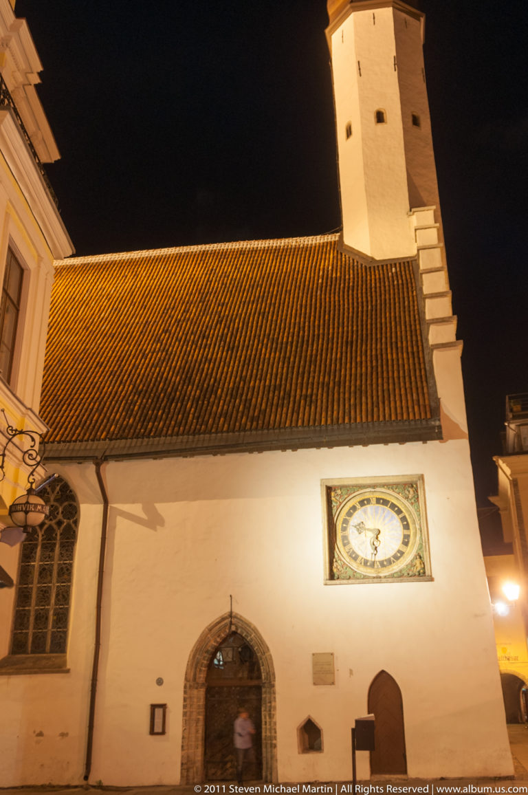 Church of the Holy Spirit at night with red tile roof, tower, arched doorway, and painted clock.
