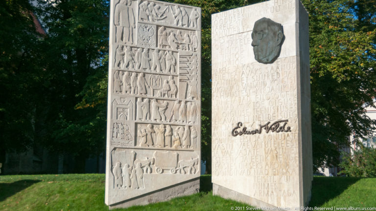 Two stone slabs of the Eduard Vilde memorial, with relief scenes, portrait medallion, text, and signature.