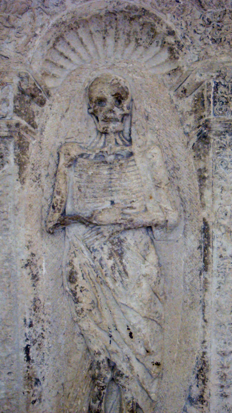 Weathered stone relief with a faint carved human figure and worn surrounding decoration.