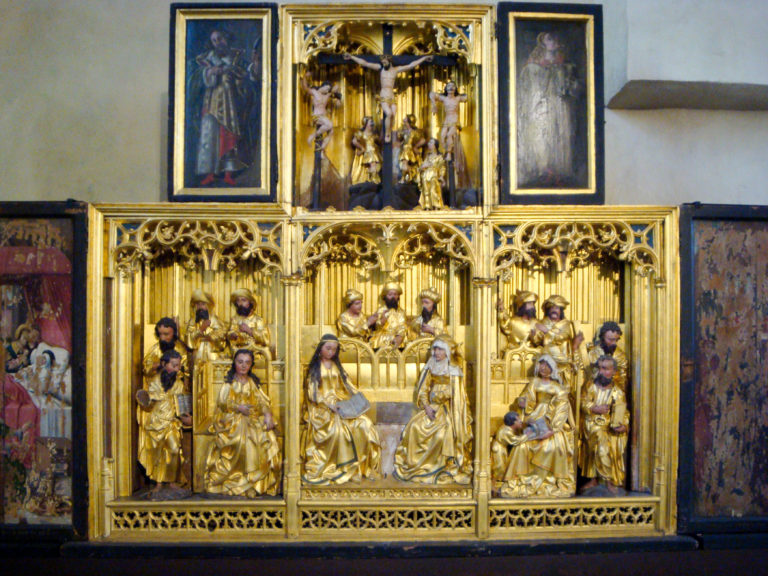 Gilded multi-tiered church altarpiece with carved religious figures, painted side panels, and intricate tracery.
