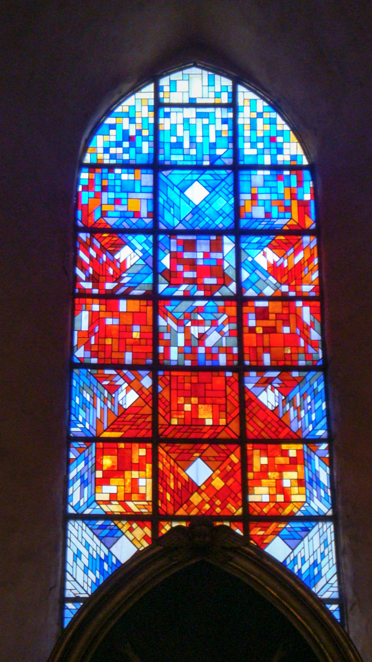 Arched stained-glass window filled with abstract geometric patterns in vivid red, blue, white, and amber.