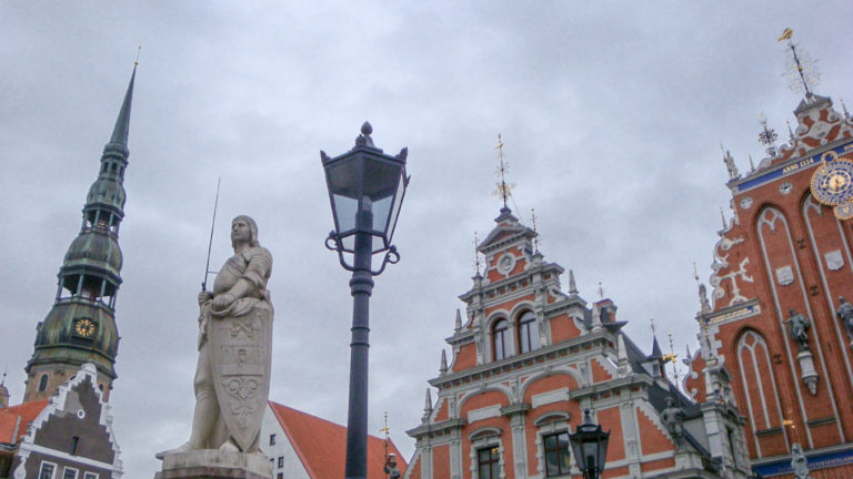Stone statue and black streetlamp before ornate red-and-white gables and a green-copper church tower.