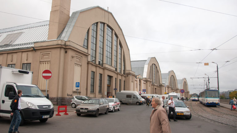 Several large arched Riga Central Market pavilions line a street with vans, cars, pedestrians, and overhead transit wires.