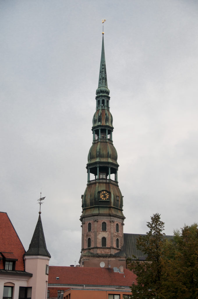 St. Peter’s Church tower with clock and tiered copper spire rising above red roofs and autumn trees.