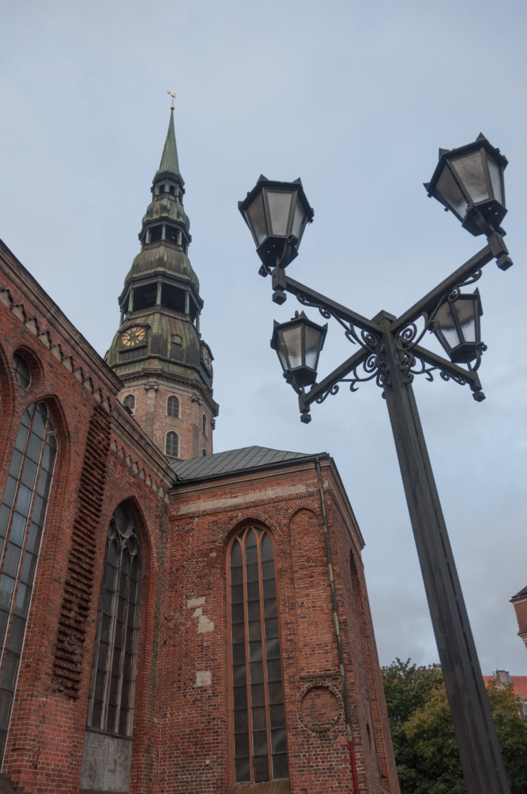 Red-brick side of St. Peter’s Church with tall Gothic windows, copper tower, and large streetlamp.