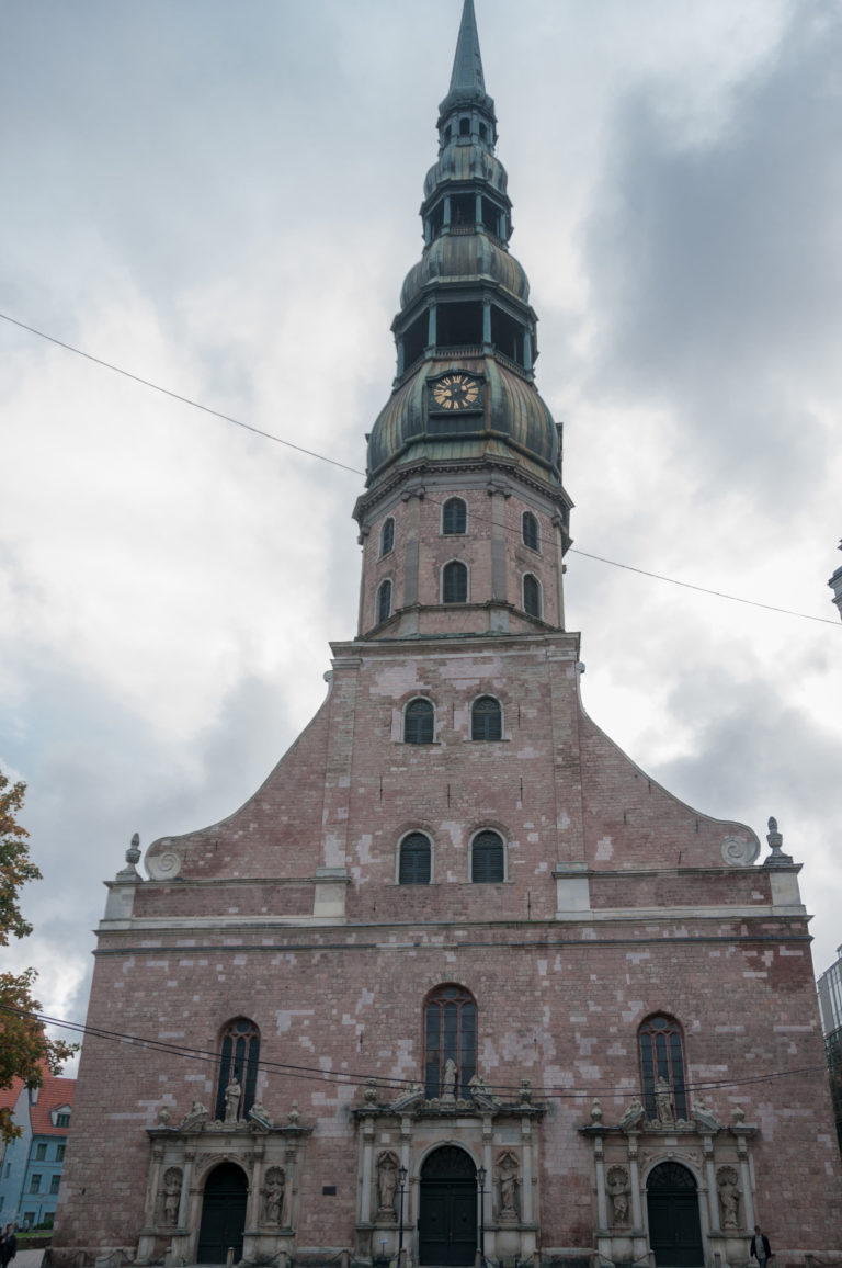 Front of St. Peter’s Church with three ornate portals, massive brick tower, clock, and tiered copper spire.
