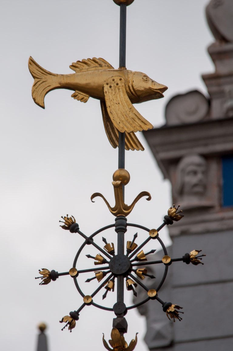 Gilded bird with outstretched wings atop scrolling black-and-gold rooftop metalwork.