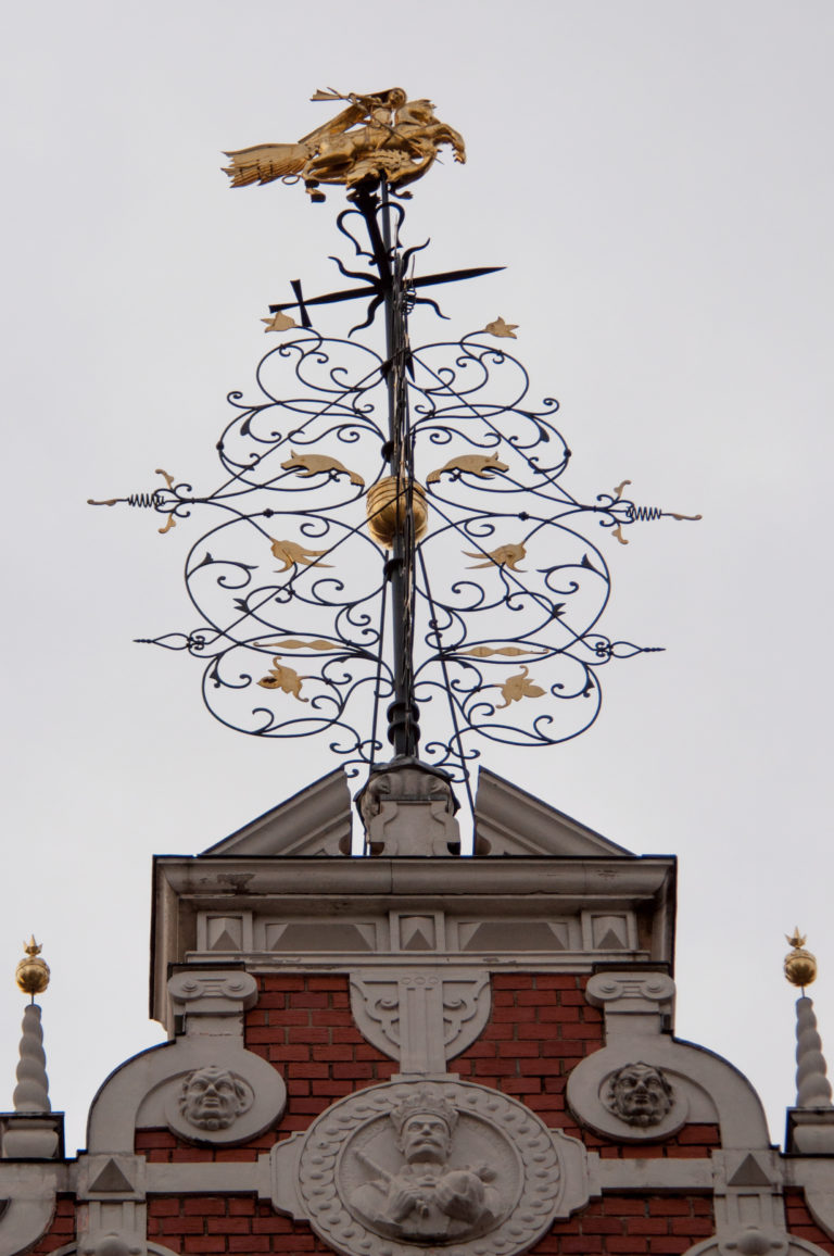 Elaborate black-and-gold wrought-metal rooftop finial with scrolling tracery above a red-brick gable.