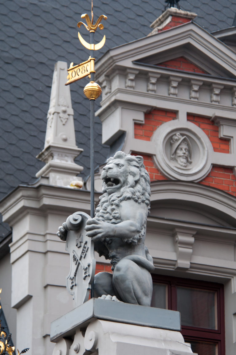 Stone lion holding a heraldic shield on the red-brick and pale-stone façade of the House of the Blackheads.