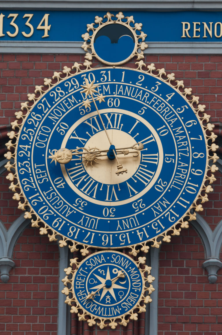 Blue-and-gold astronomical clock with Roman numerals, calendar rings, and smaller celestial dial below.