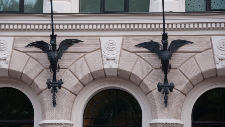 Two black metal dragon brackets mounted symmetrically above arched windows on a pale facade.
