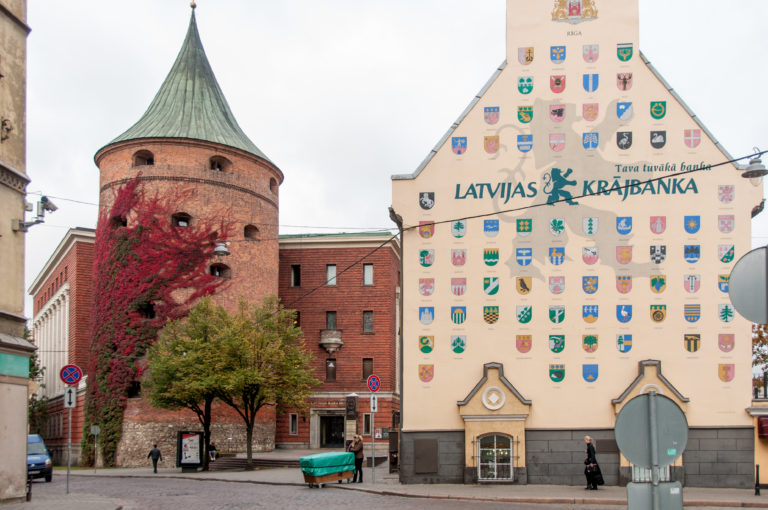 Powder Tower beside a tall gabled facade covered with colorful Latvian municipal coats of arms.