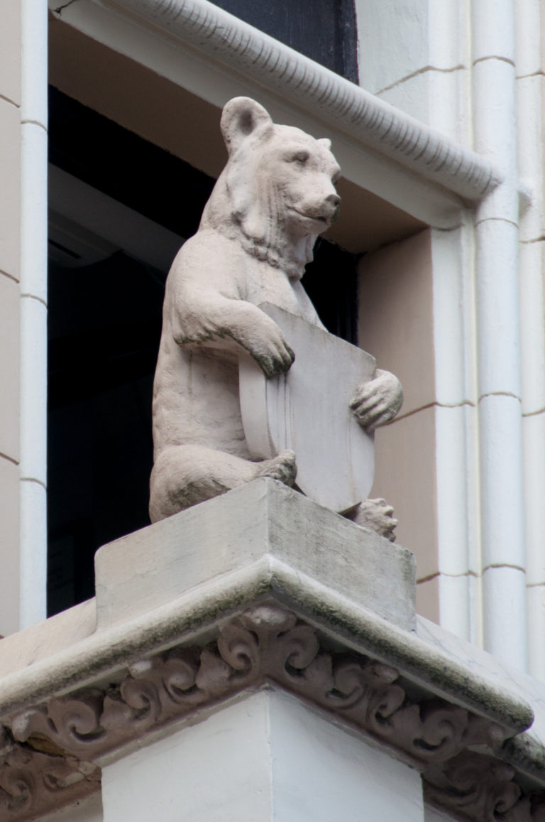 Carved stone bear holding a shield on a projecting ledge of a pale historic facade.