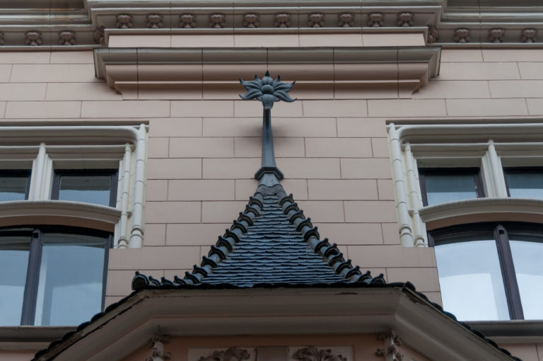 Steep shingled canopy with scalloped trim and a dark ornamental finial between windows.