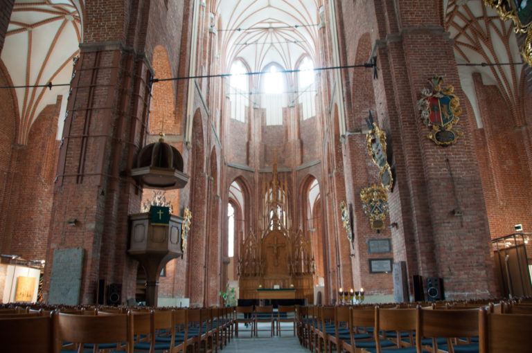 Brick Gothic church interior with tall piers, pointed arches, pulpit, heraldic memorials, and altar.