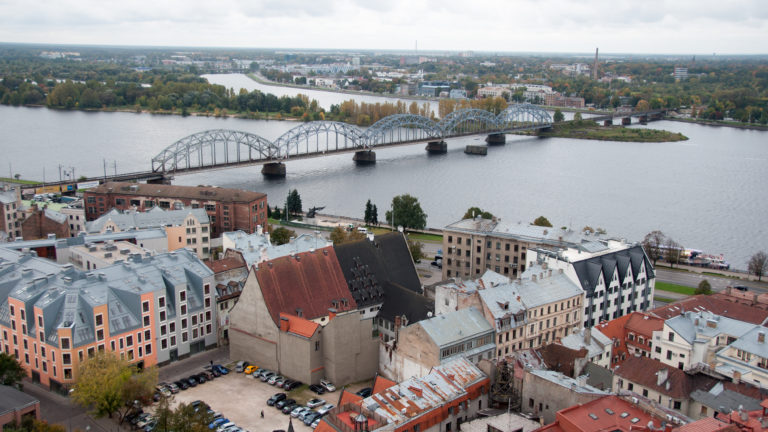 Steel arched railway bridge crossing the Daugava River beyond Riga rooftops.