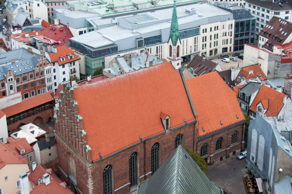 Brick Gothic church with steep red-tile roof and stepped gable surrounded by dense rooftops in central Riga.