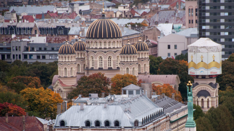 Nativity of Christ Cathedral seen from above with the Freedom Monument foreground and modern Riga buildings behind.
