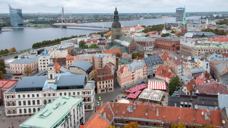 High-angle view across colorful Old Riga gables, narrow streets, red-tile roofs, and taller towers beyond.