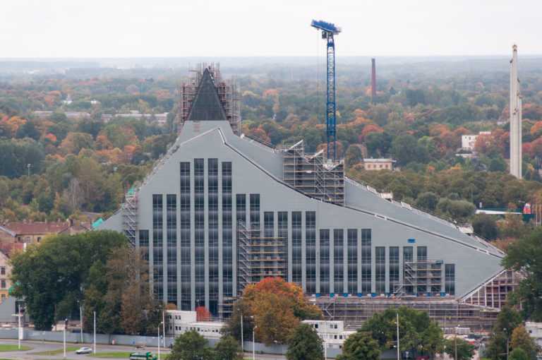 National Library of Latvia under construction, with scaffolding on its steep angular roof and long glazed facade.