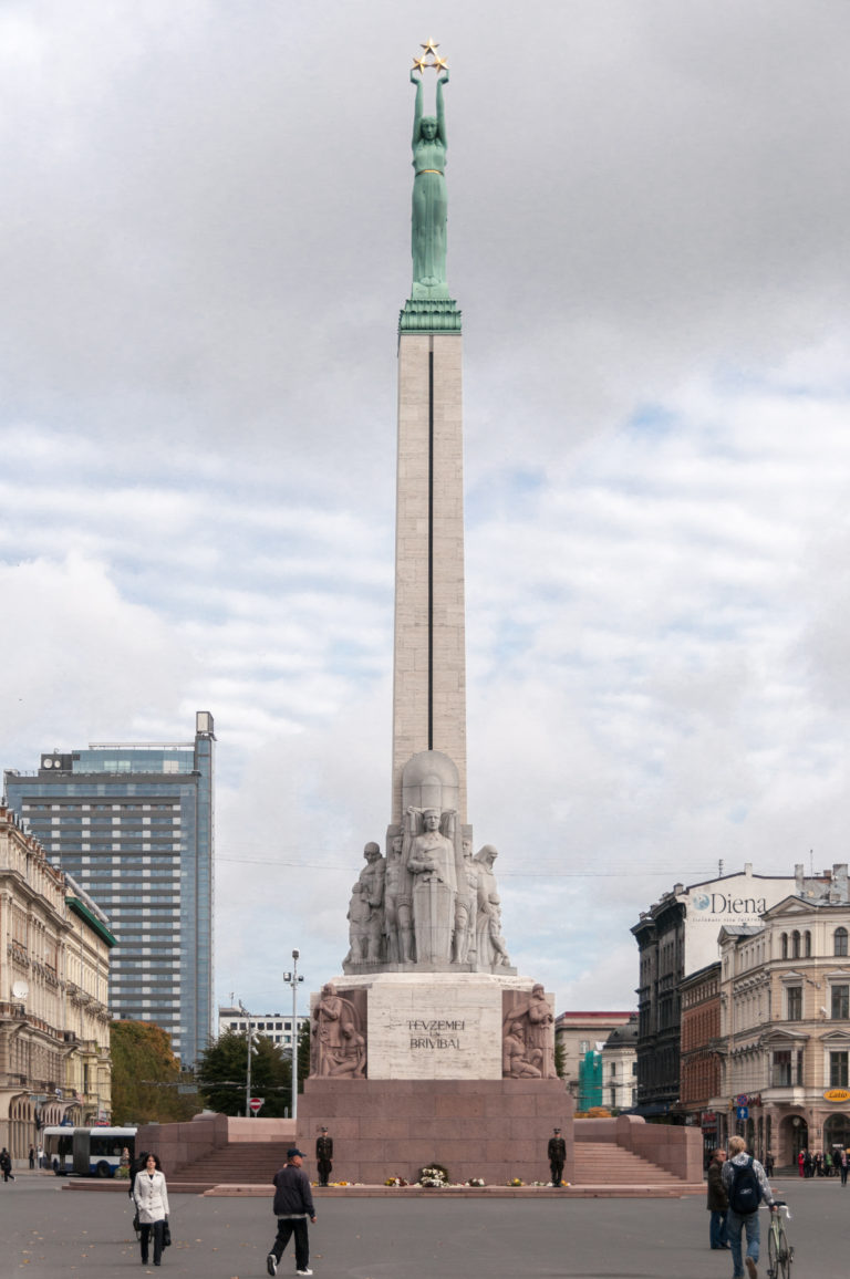 Full Freedom Monument in Riga rising above its sculpted base with pedestrians crossing the square below.